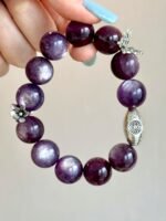 Flatlay of lepidolite bracelet, silver oval charm and flower pendant match, water-metal energy shows warm texture