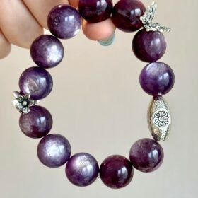 Flatlay of lepidolite bracelet, silver oval charm and flower pendant match, water-metal energy shows warm texture