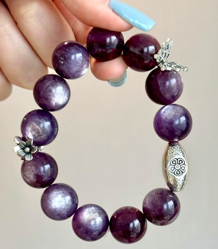 Flatlay of lepidolite bracelet, silver oval charm and flower pendant match, water-metal energy shows warm texture