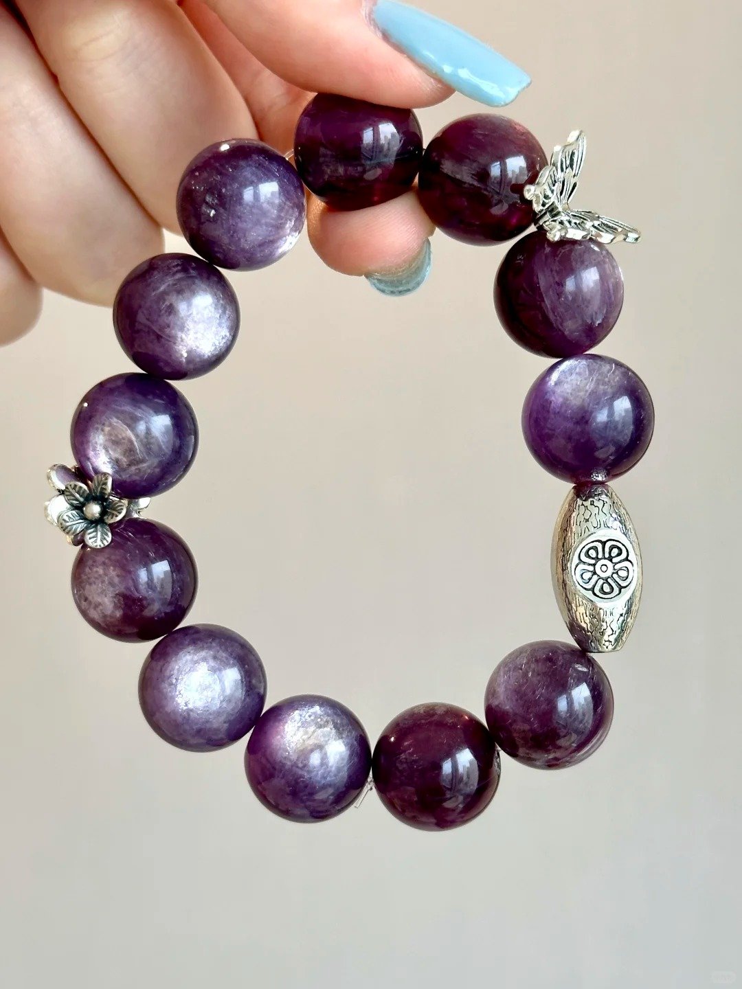 Flatlay of lepidolite bracelet, silver oval charm and flower pendant match, water-metal energy shows warm texture