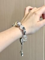 Multi-crystal bracelet on wrist, silver bell charm sways, metal-water energy builds serene aura