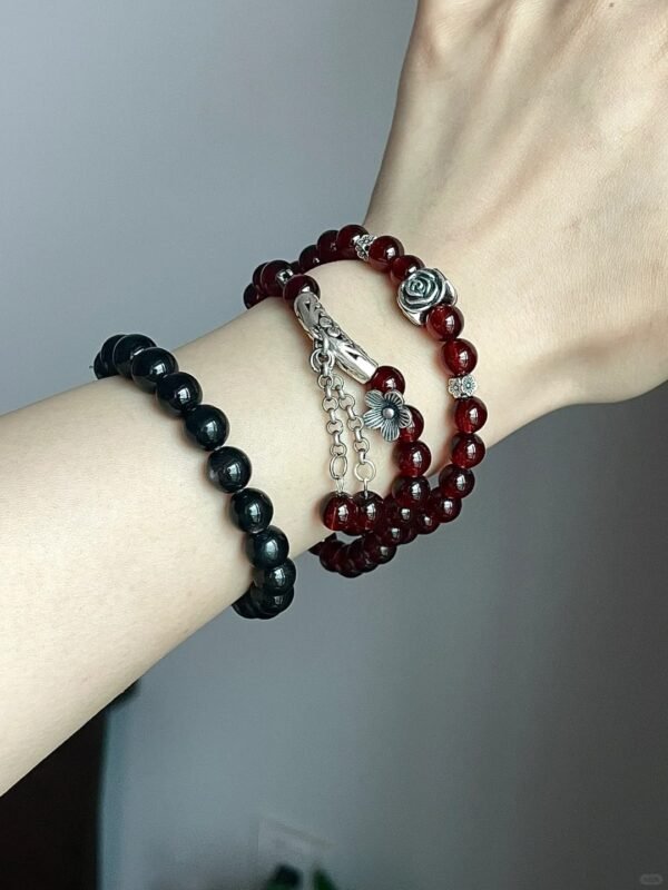 Holding single-strand garnet bracelet, silver carved pendant chain, fire-metal energy hidden in red hues