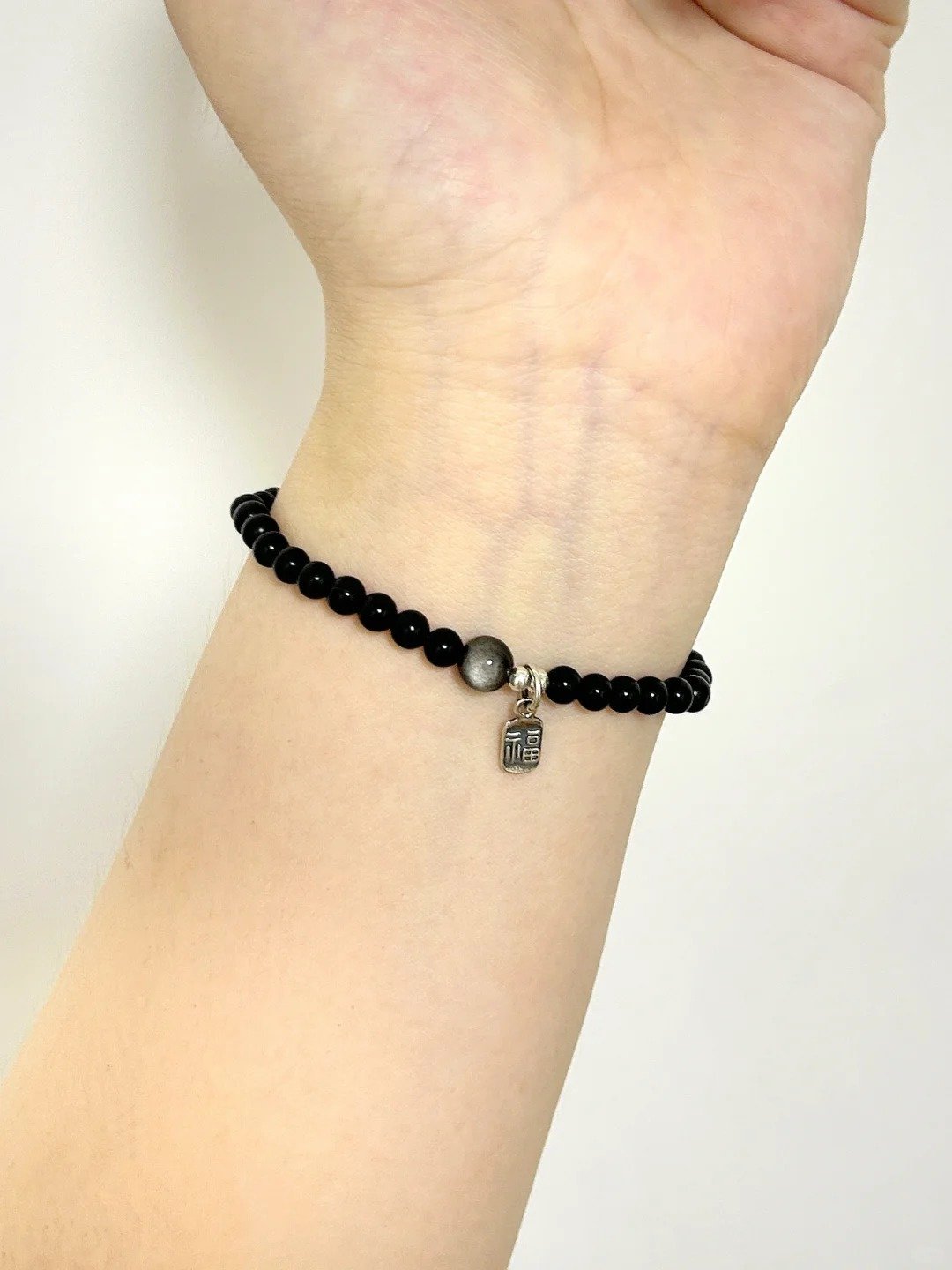 Obsidian bracelet on wrist, delicate bead design, water-metal energy building protection aura