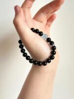 Holding aquamarine & obsidian double-strand bracelet, layered design showing style, water-metal synergy building aura