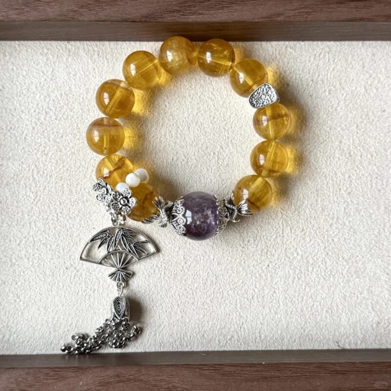 Golden rutilated quartz bracelet displayed by ancient books, silver fan pendant shows antique charm, metal-fire-earth energy in vintage vibe