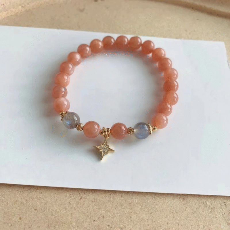 Flatlay of orange moonstone bracelet, gold star charm in center, fire-metal energy in vintage charm