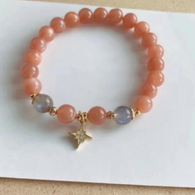 Flatlay of orange moonstone bracelet, gold star charm in center, fire-metal energy in vintage charm