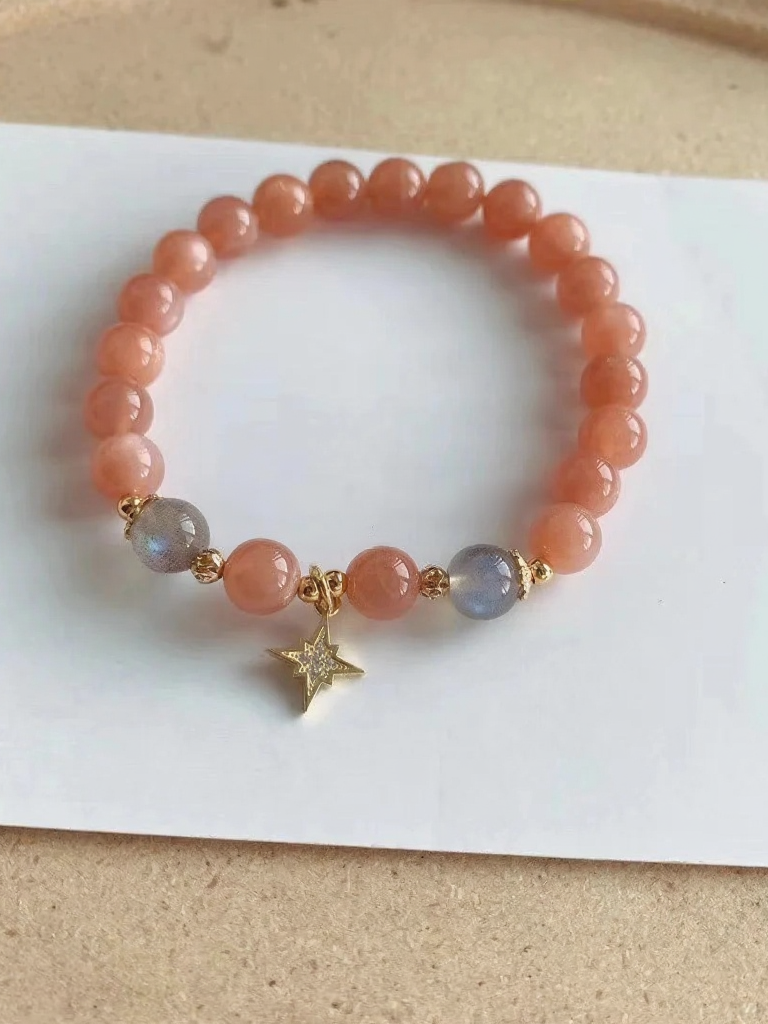 Flatlay of orange moonstone bracelet, gold star charm in center, fire-metal energy in vintage charm