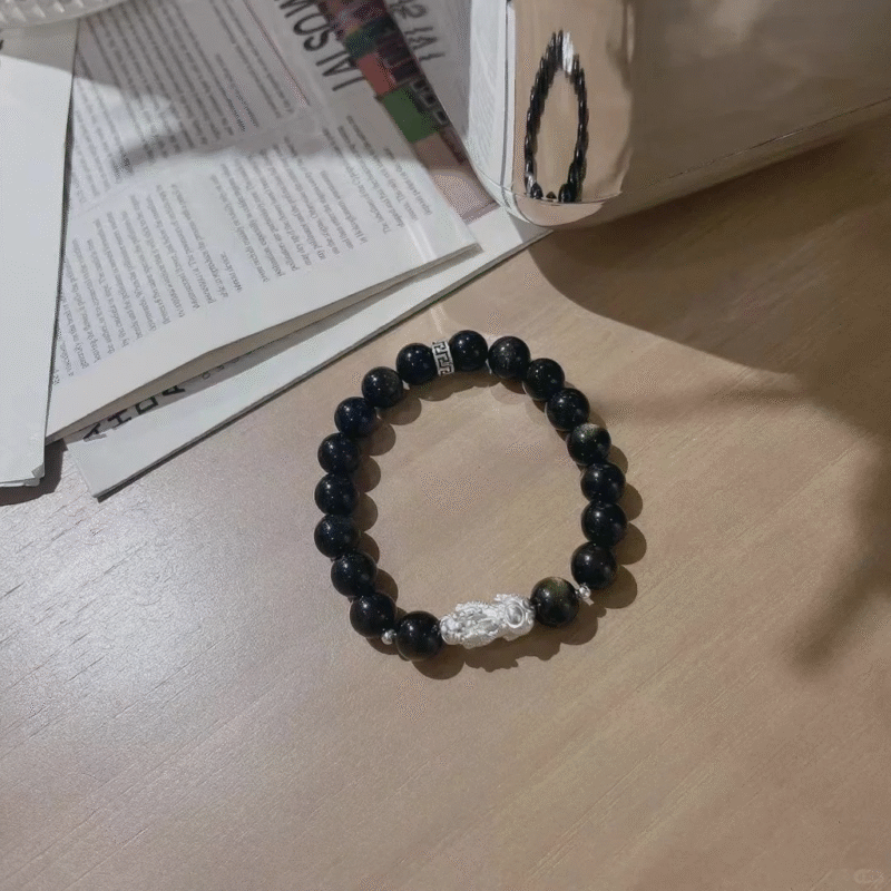 Flatlay of golden obsidian bracelet, 999 silver pixiu in center, water-metal energy locks wealth