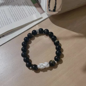 Flatlay of golden obsidian bracelet, 999 silver pixiu in center, water-metal energy locks wealth