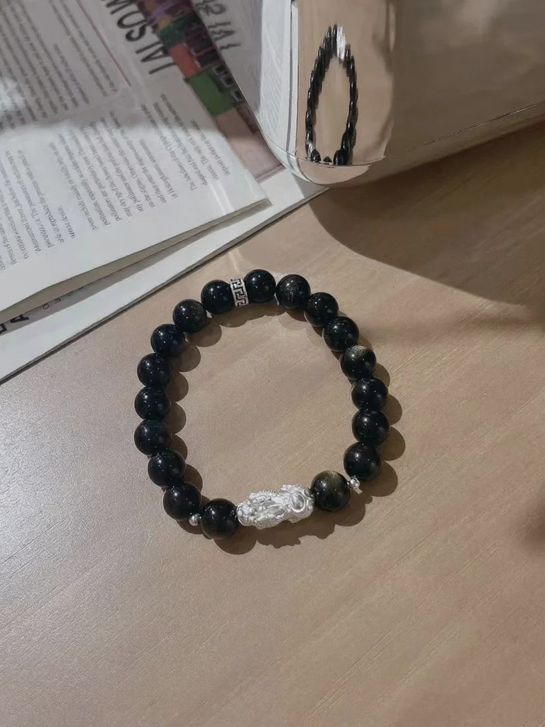 Flatlay of golden obsidian bracelet, 999 silver pixiu in center, water-metal energy locks wealth
