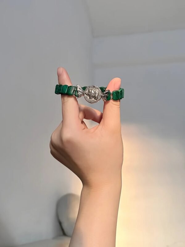 Malachite bracelet on finger, silver flower charm shows craft, wood-metal energy builds finger aura