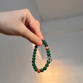 Holding single-strand malachite bracelet with red agate spacers and silver flower charm, wood-fire-metal energy blooms