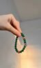 Holding single-strand malachite bracelet with red agate spacers and silver flower charm, wood-fire-metal energy blooms