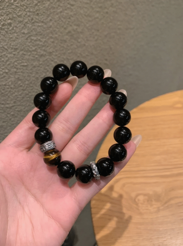 Hand Displaying 10mm Black Obsidian & Yellow Tiger’s Eye Bracelet, Water-Metal-Earth Energy Weaves Courage Field