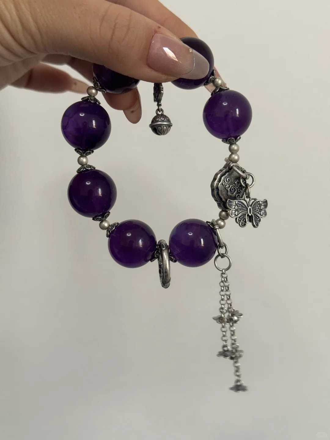 Close-up of Uruguay Amethyst bracelet with silver butterfly and bell accents, showcasing water-metal energy resonance